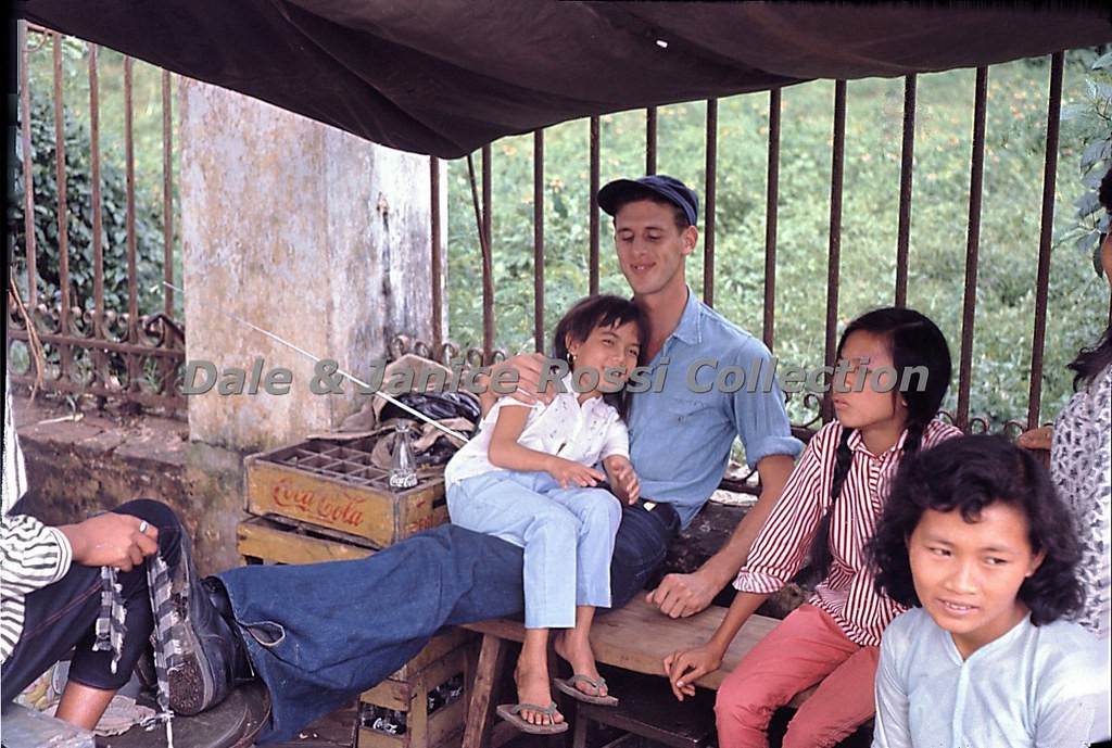 Một quầy giải khát vỉa hè cùng anh khách tây và trẻ em Việt, sự thân thiện được biểu hiện rõ bởi nụ cười trên môi